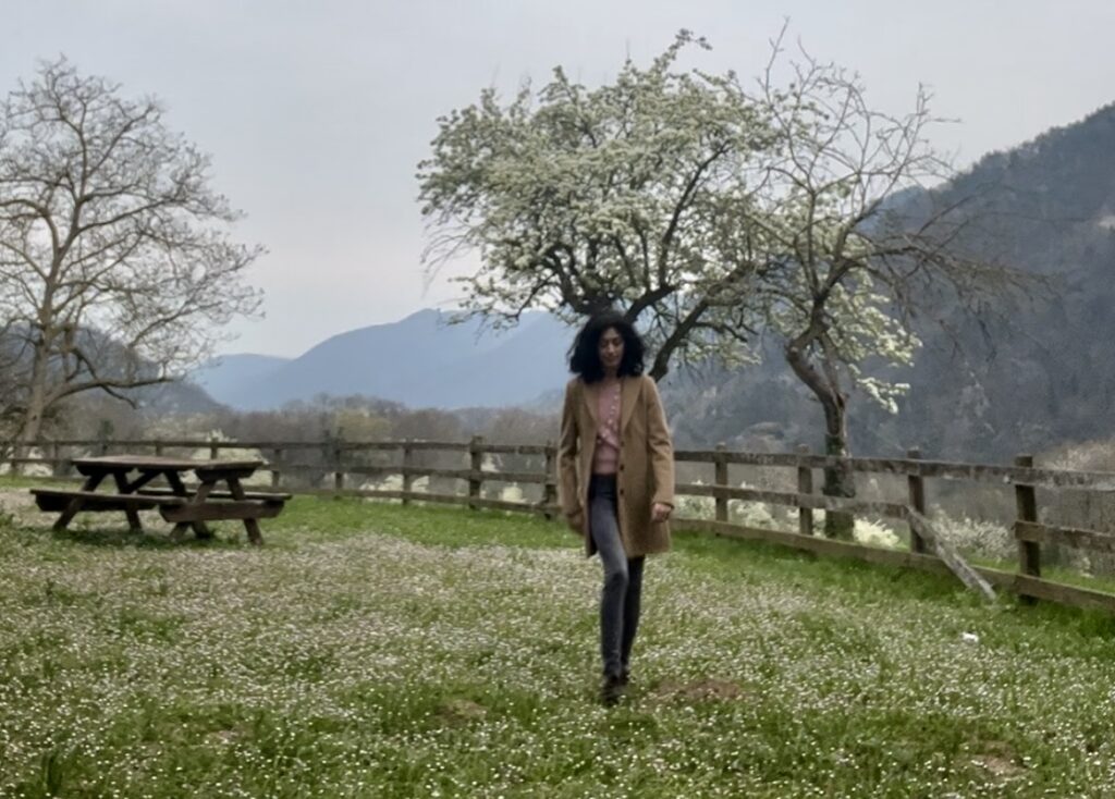 L'autrice di Venerdì (In)Versi Beatrice Condorelli mentre cammina su un prato fiorito circondato dalle montagne
